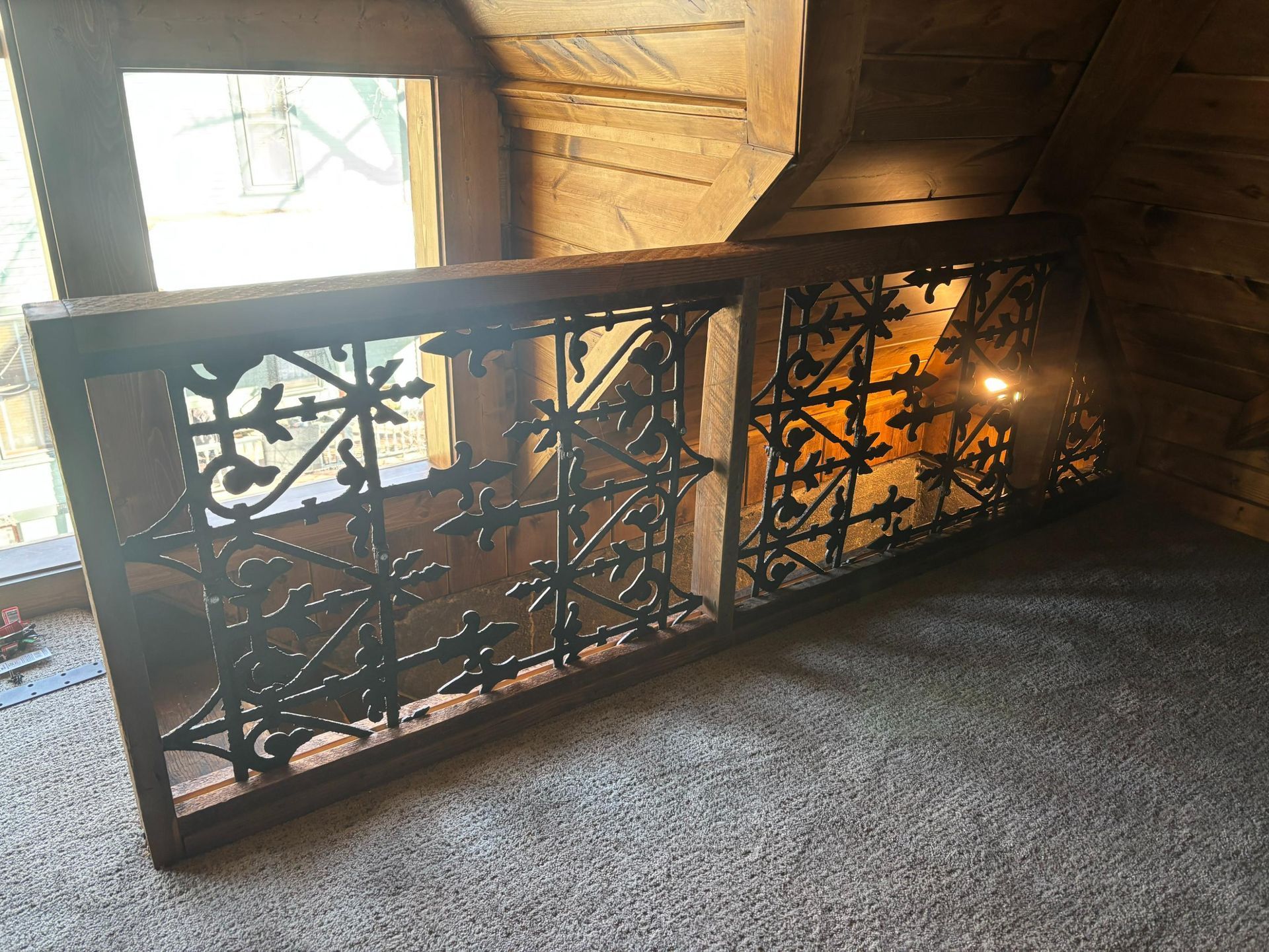 Decorative metal railing indoors by a sunlit window, with warm light and carpeted floor