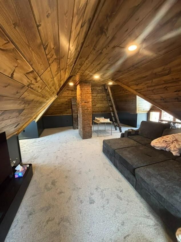 Attic living room with sloped wood ceiling, gray sectional sofa, and white carpet.