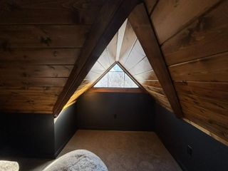 Attic nook with wood-paneled sloped ceiling, triangular window, and a small round cushion on the floor