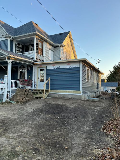 Two-story house under renovation with blue garage door, stone exterior, and a gravel driveway.