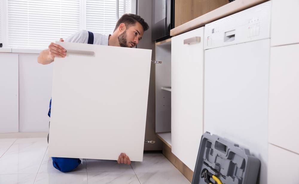 young handyman fixing sink door in kitchen