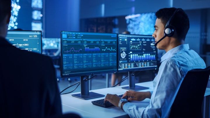 A man wearing a headset is sitting in front of two computer monitors.
