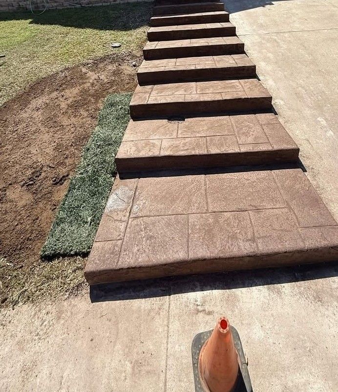 Brown stepped walkway blocks leading up a concrete driveway beside a patchy lawn.