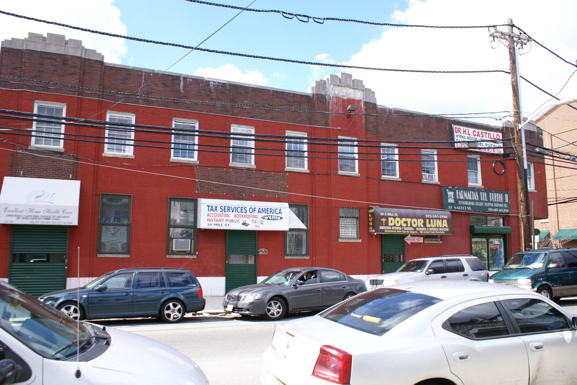 Red brick commercial building with storefront signs and parked cars along a street
