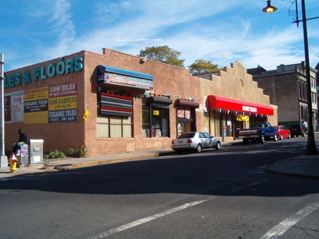 Brick storefronts on a sunny street corner, with parked cars and colorful awnings.