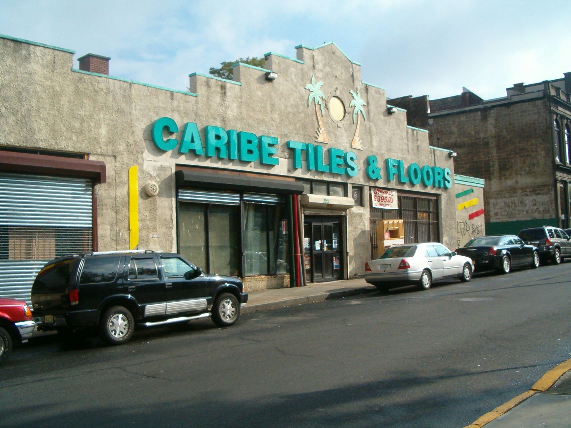 Storefront of Caribe Tiles & Floors on a street, with parked cars and a stone facade