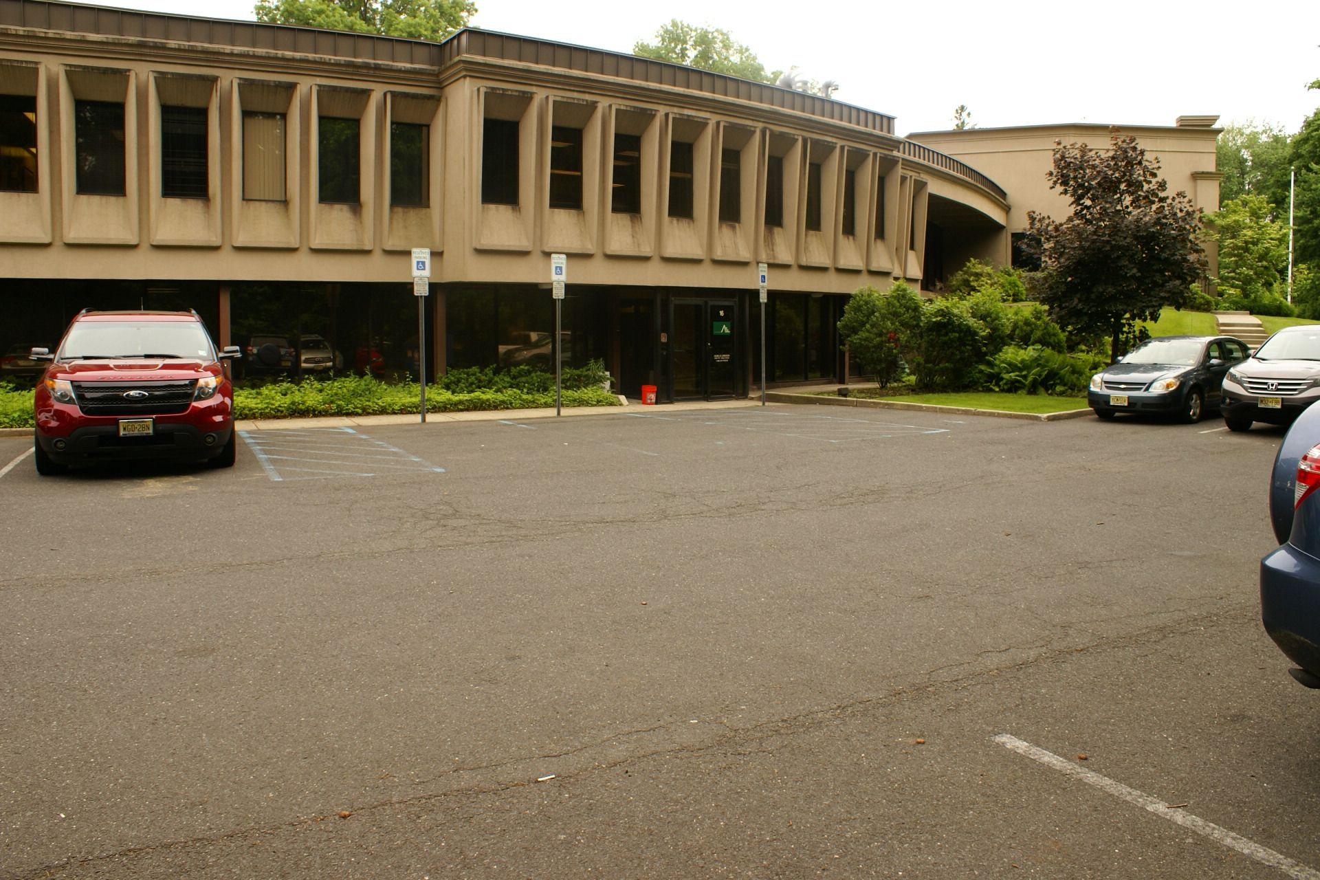 Parking lot with several cars in front of a curved tan building and greenery