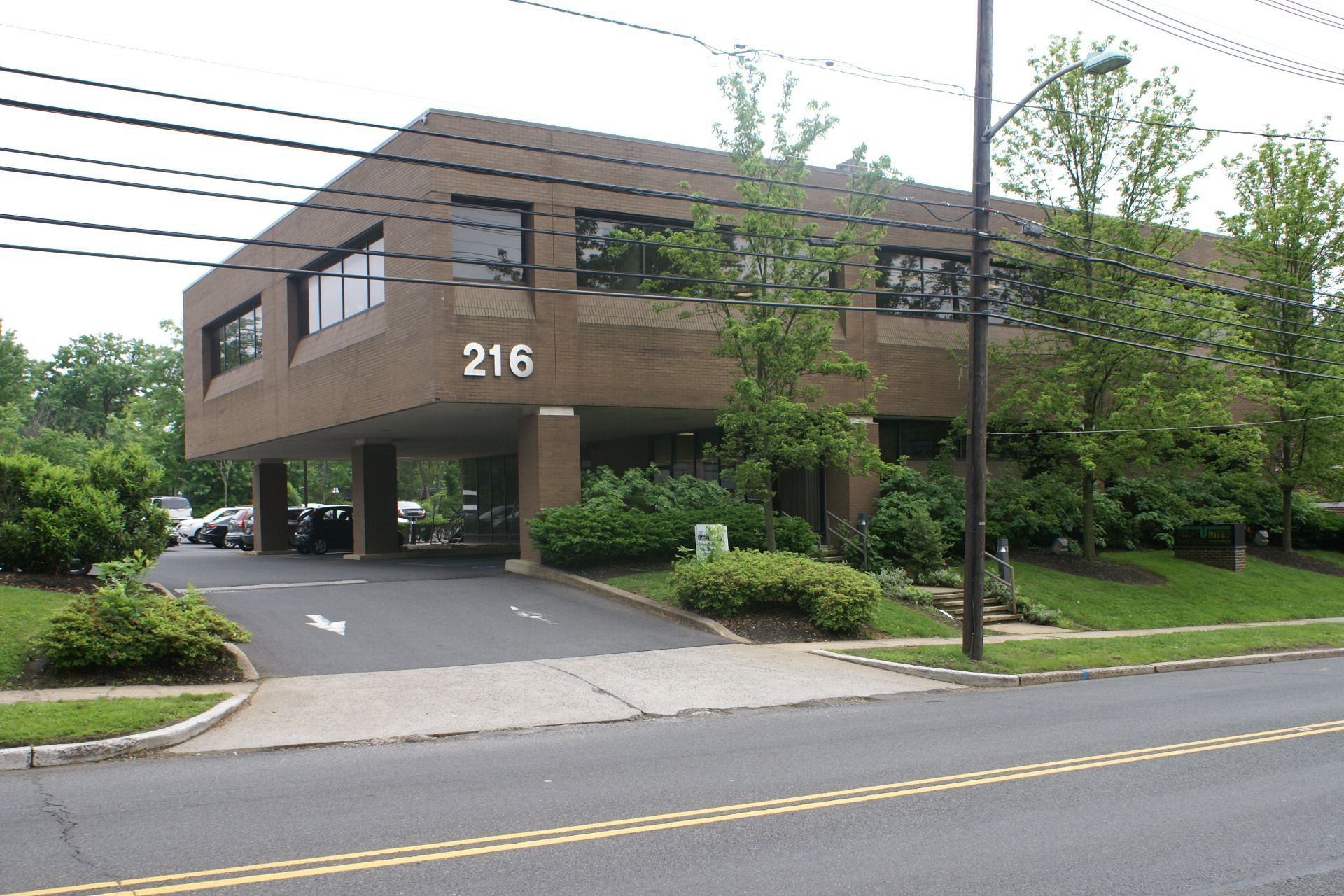 Office building with number 216, brown exterior, trees, and a driveway beside a street
