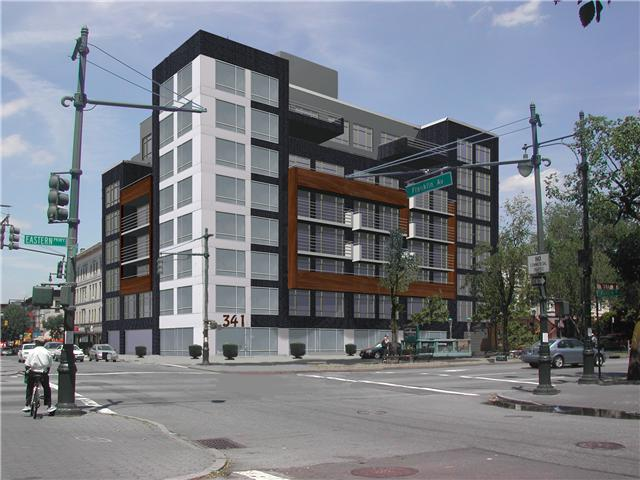 Modern gray-and-orange apartment building on a city street corner with traffic lights and pedestrians