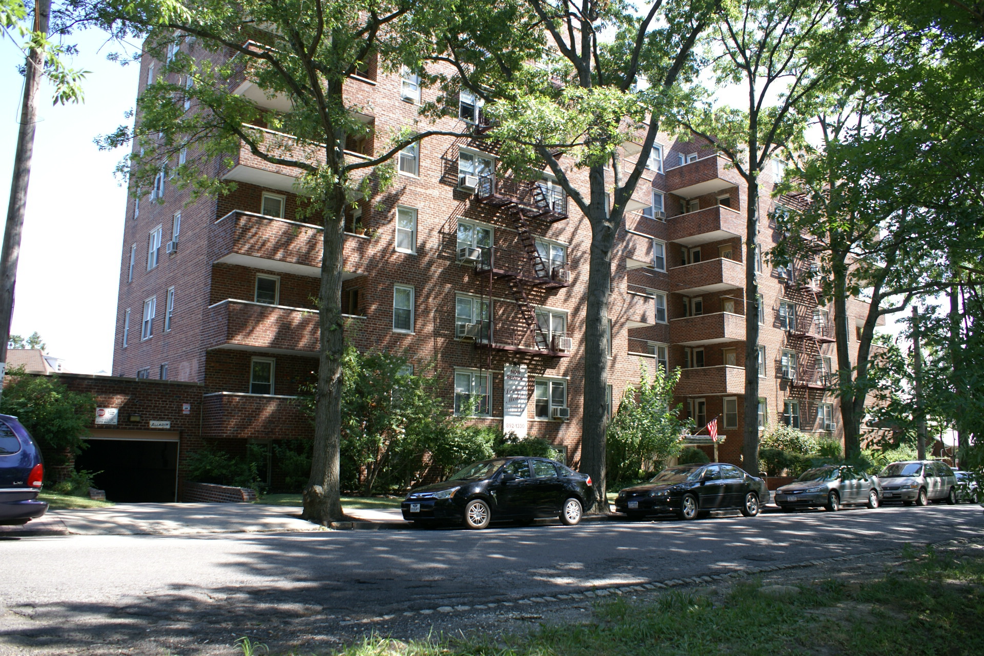 Brick apartment buildings along a tree-lined street with parked cars in front