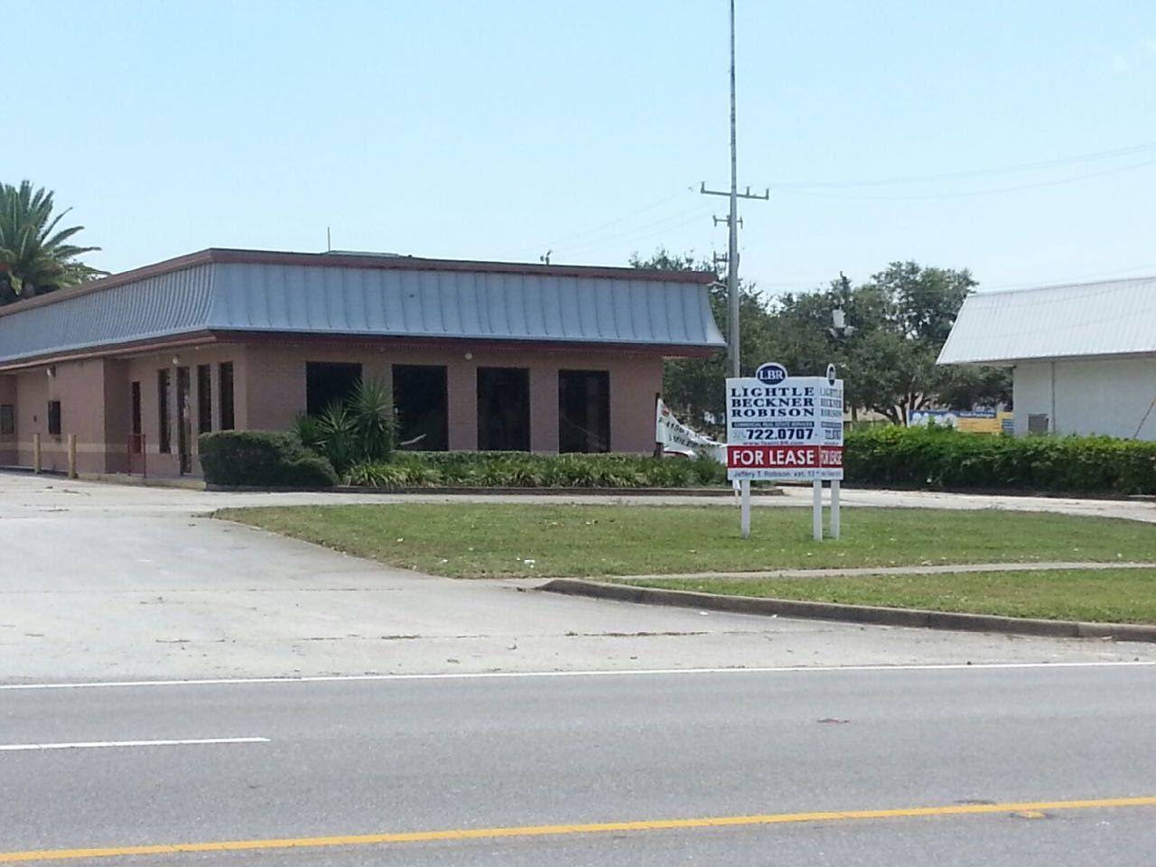 Low brick building with a sign beside a road, under a clear blue sky
