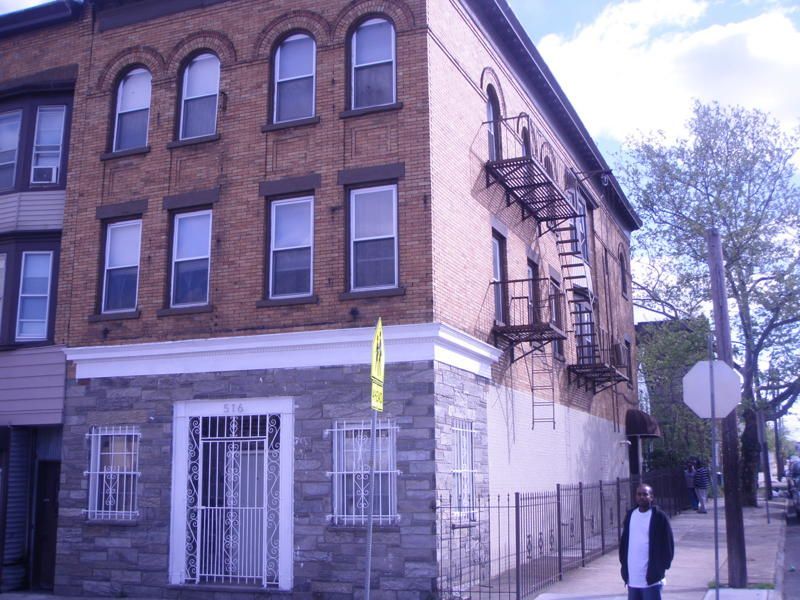 Brick building on a city street with a person walking by and fire escape stairs on the side.
