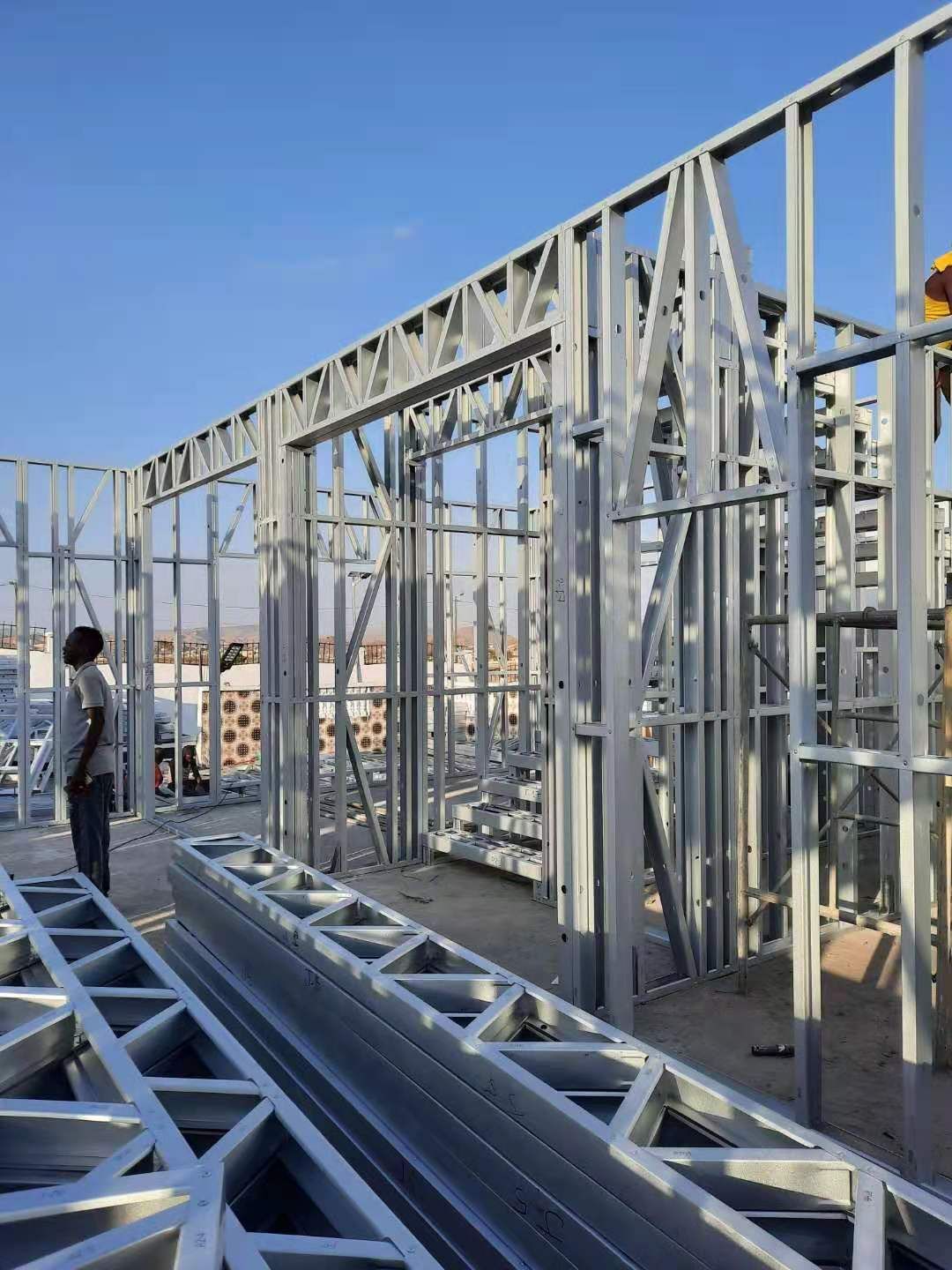 Steel framing of a building under construction, with workers and a blue sky in the background