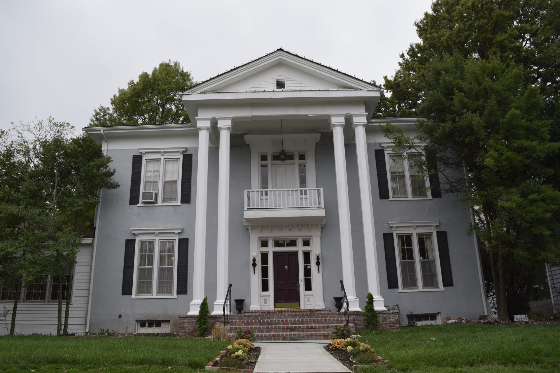 Gray colonial-style house with white columns, shutters, and a front lawn