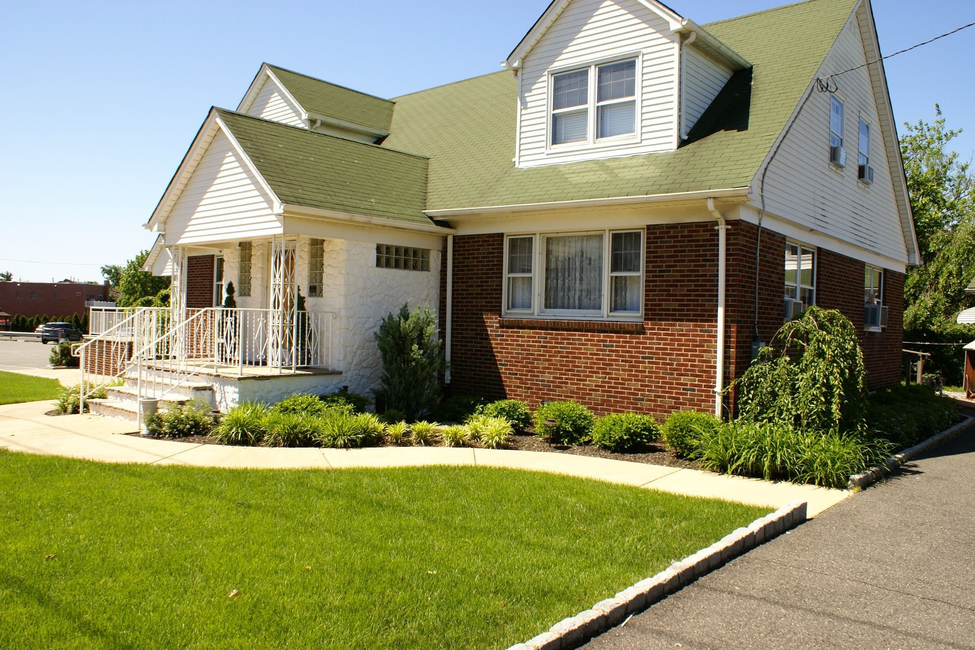 White house with green roof, front porch, and neatly landscaped lawn on a sunny day