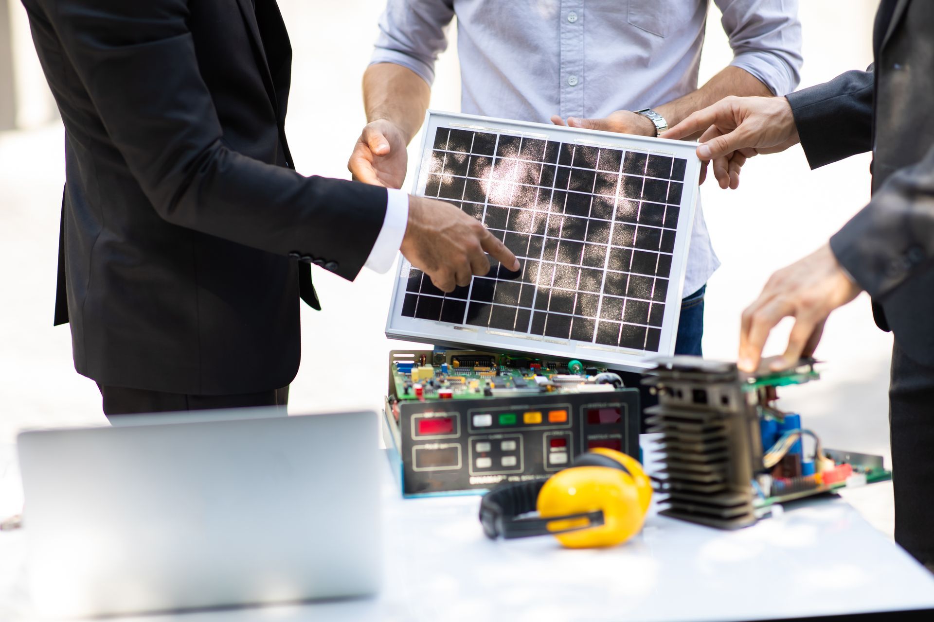 People inspecting a solar panel prototype on a table with technical equipment and a yellow hard hat