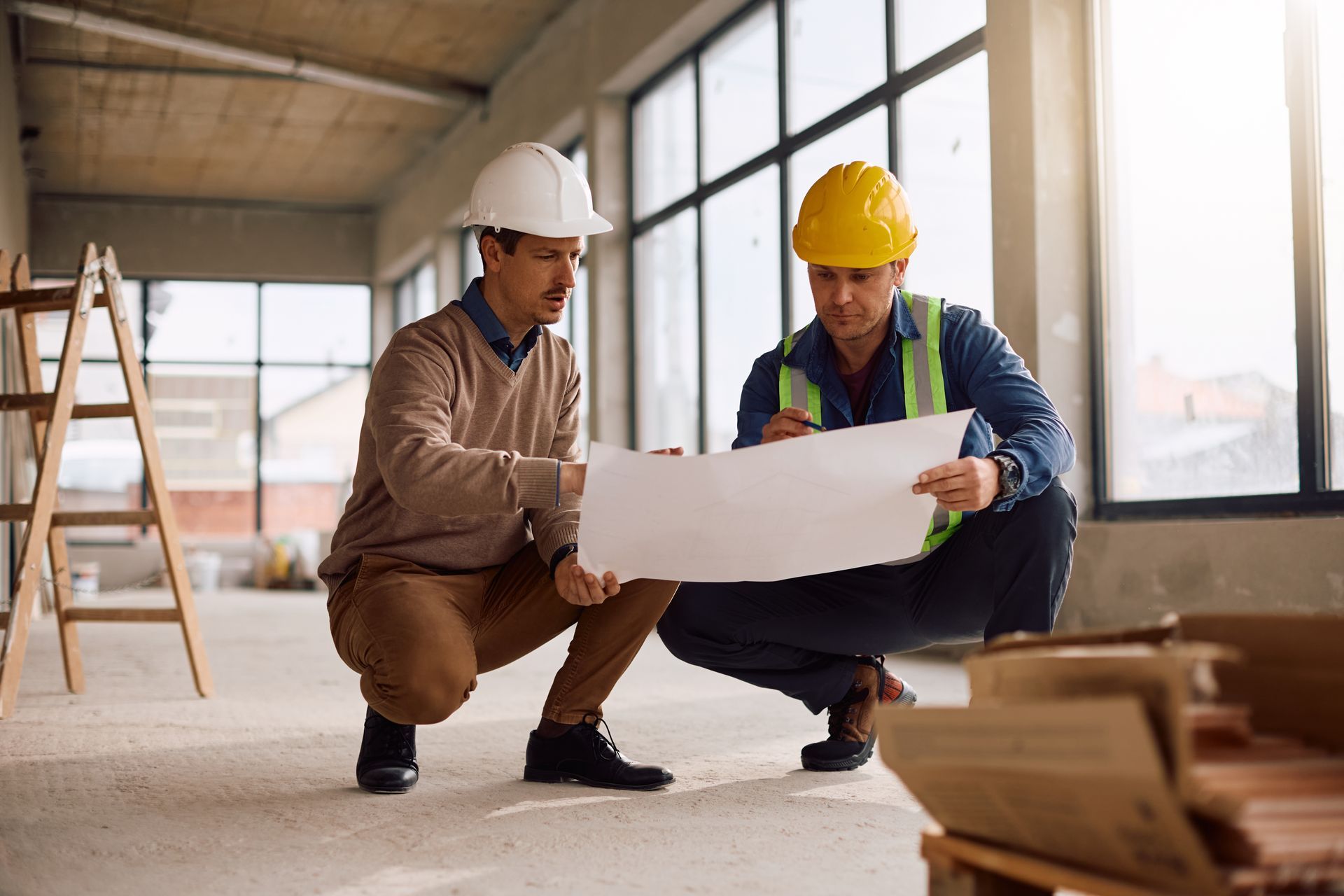 Two construction workers in hard hats reviewing blueprints at a building site