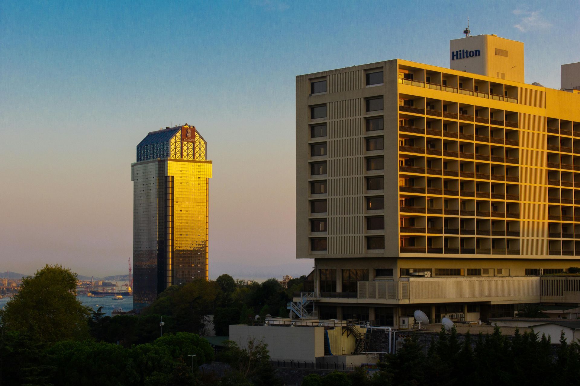 Sunlit city skyline with a tall dome-topped tower and a modern high-rise at sunset