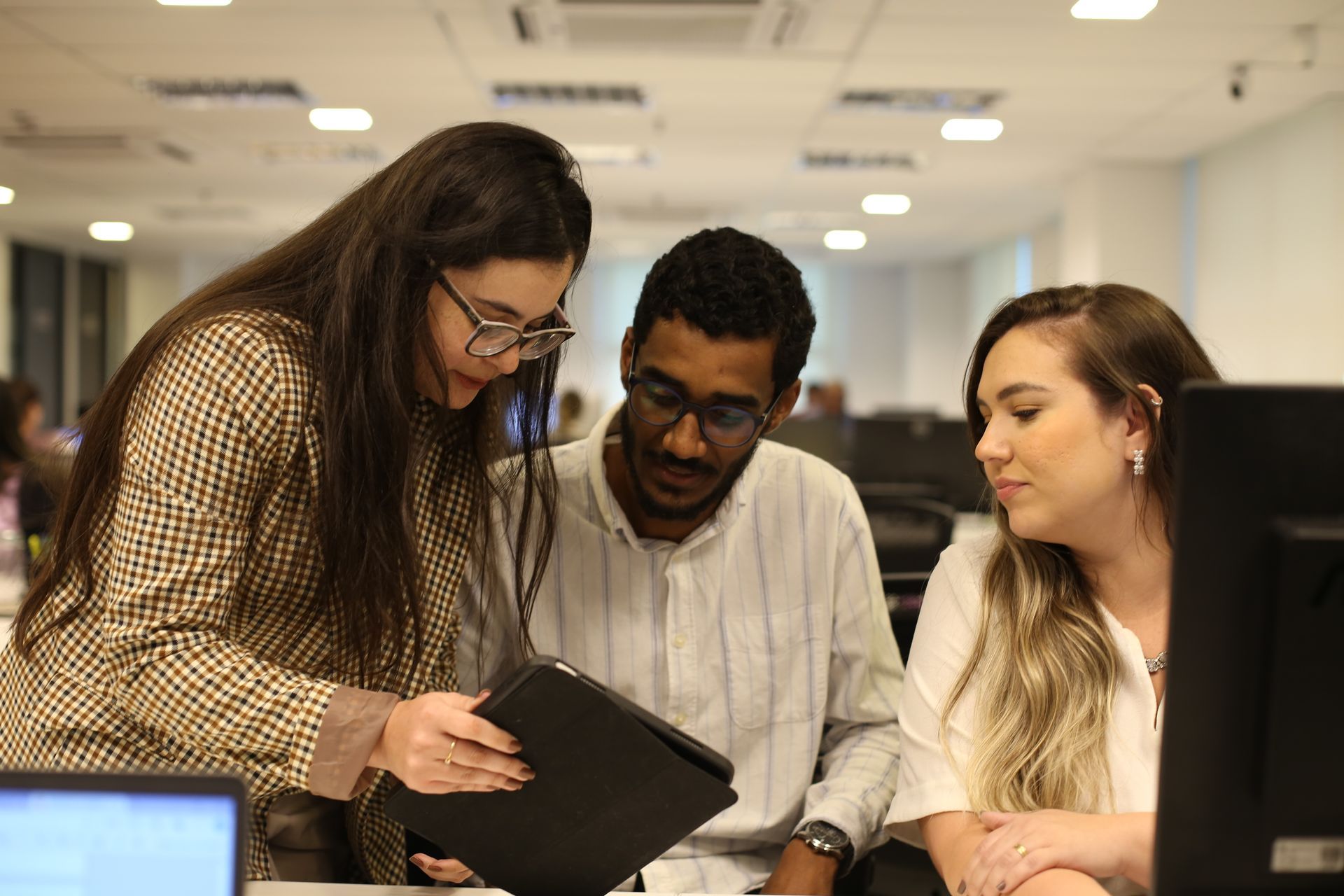 Três colegas de trabalho revisando juntos um tablet em um escritório.