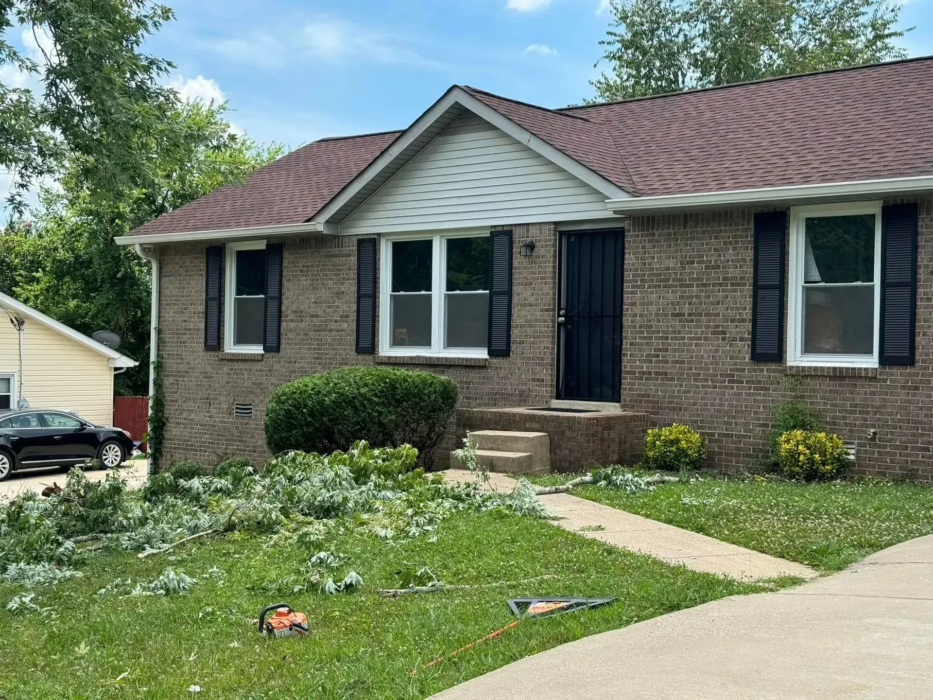 A brick house with black shutters, a dark front door, and trimmed shrubbery scattered across the front lawn.