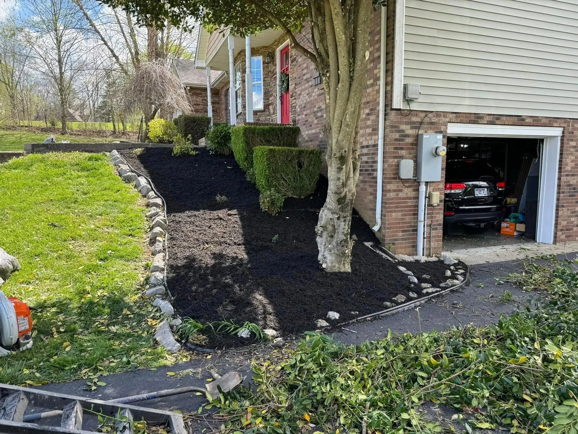 A brick house exterior with a landscaped garden bed containing mulch and shrubs next to a garage entrance.