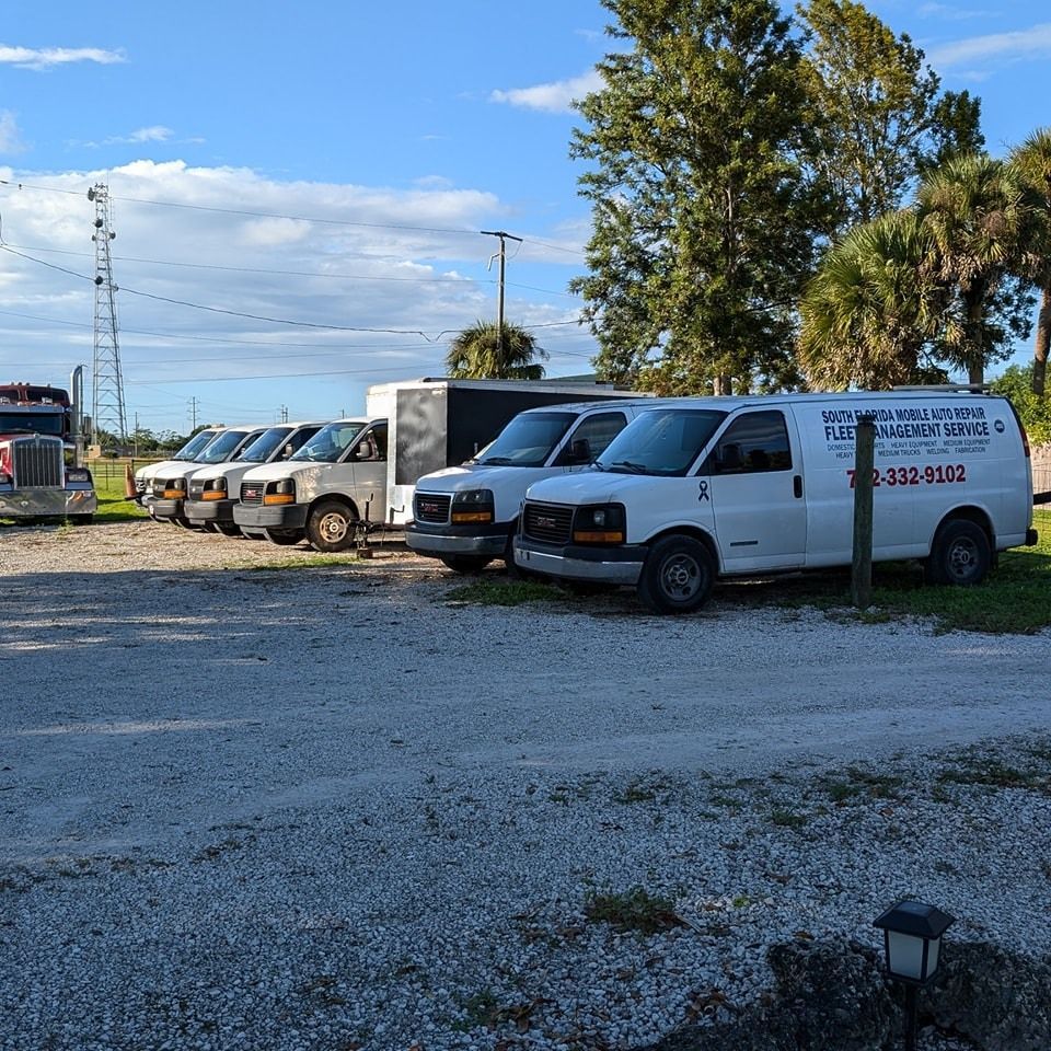 A row of white vans are parked in a gravel lot.