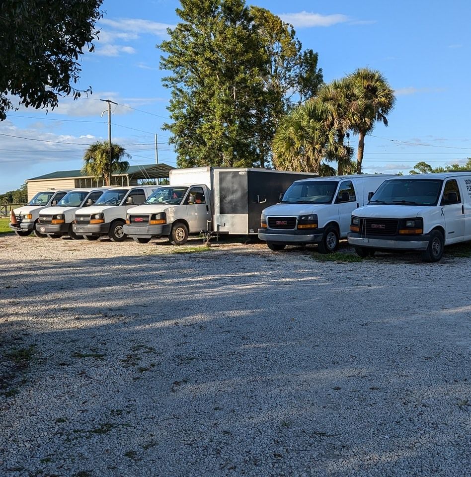 A row of vans are parked in a gravel lot.