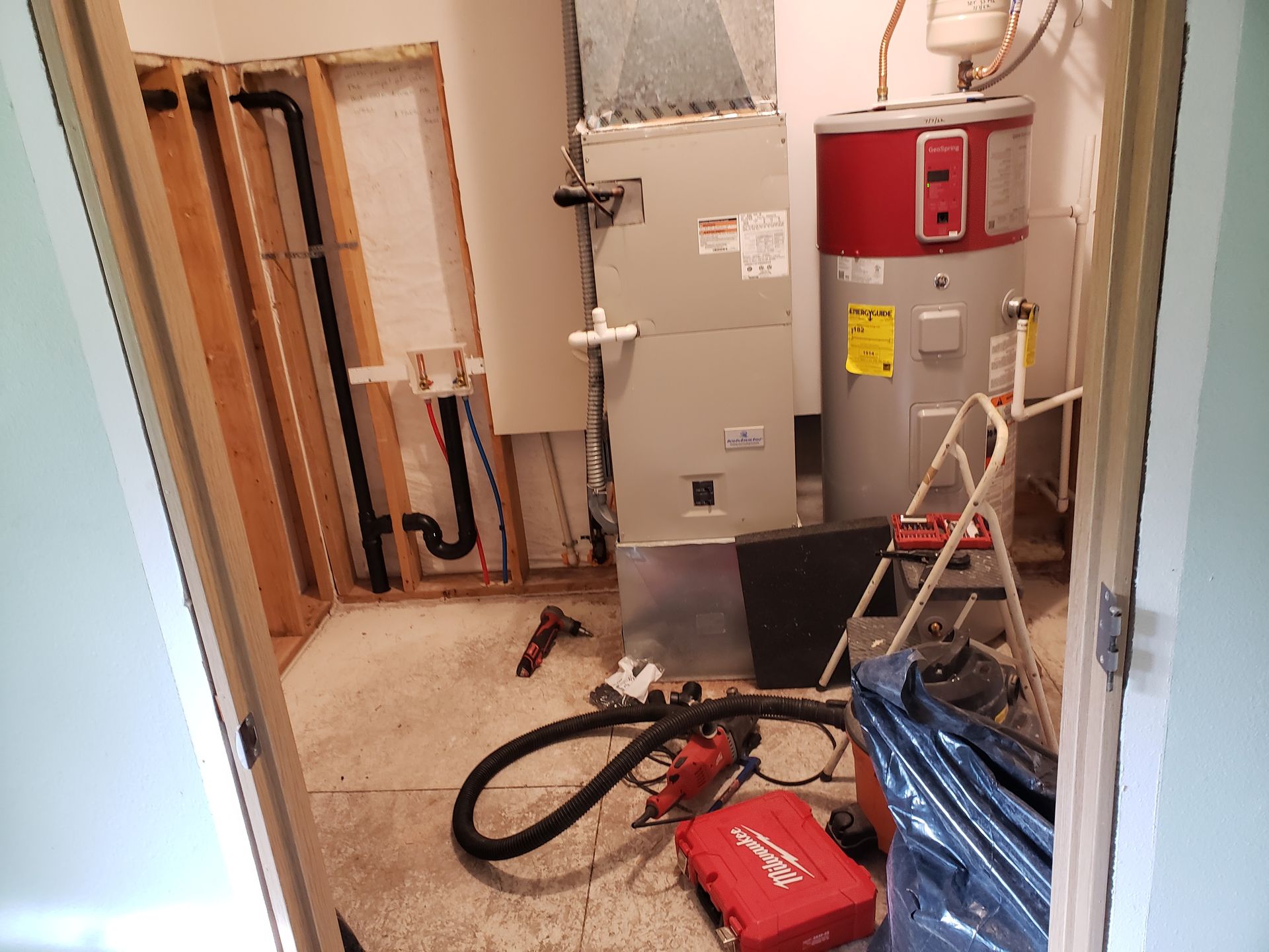 Utility room with water heater, furnace, exposed pipes, and tools on the floor during repair work