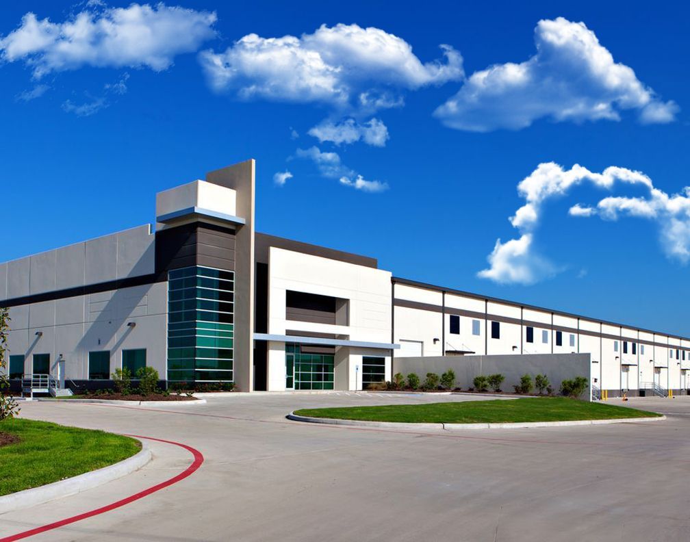Warehouse building with blue sky, clouds, and paved driveway.