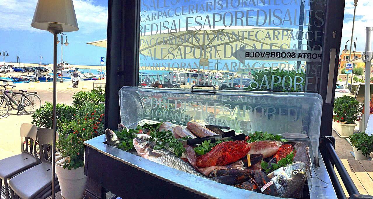 Esposizione di pesce fresco in un ristorante sul mare, con vista sull'oceano e sulla strada.