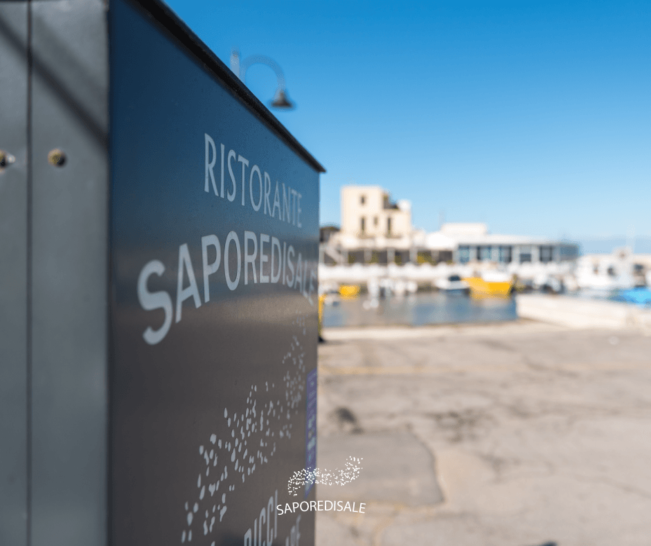 Insegna per il ristorante "Ristorante SaporediSale" vicino a un porto; sfondo sfocato di edifici e barche.