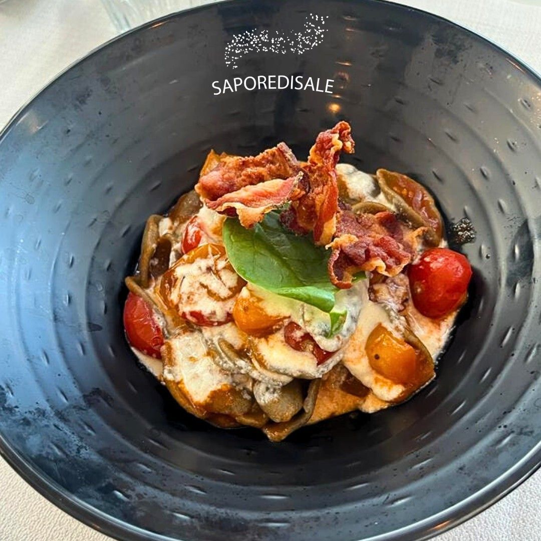 Piatto di pasta con pomodori, pancetta e basilico in una ciotola nera.