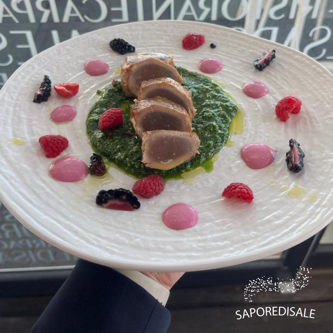 Un piatto di carne affettata su purea verde, guarnito con salsa rosa e frutti di bosco.