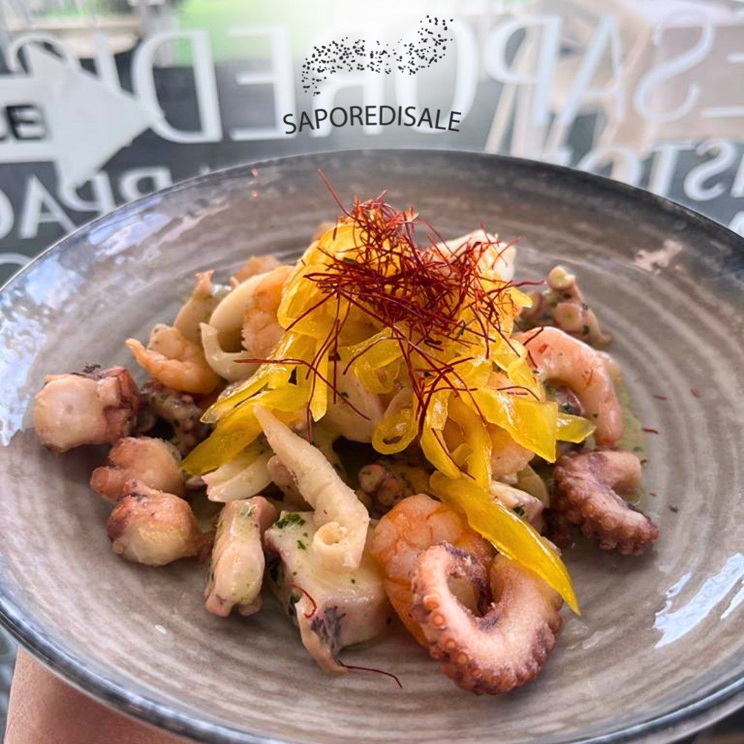 Insalata di mare in una ciotola grigia guarnita con fette gialle e fili rossi.