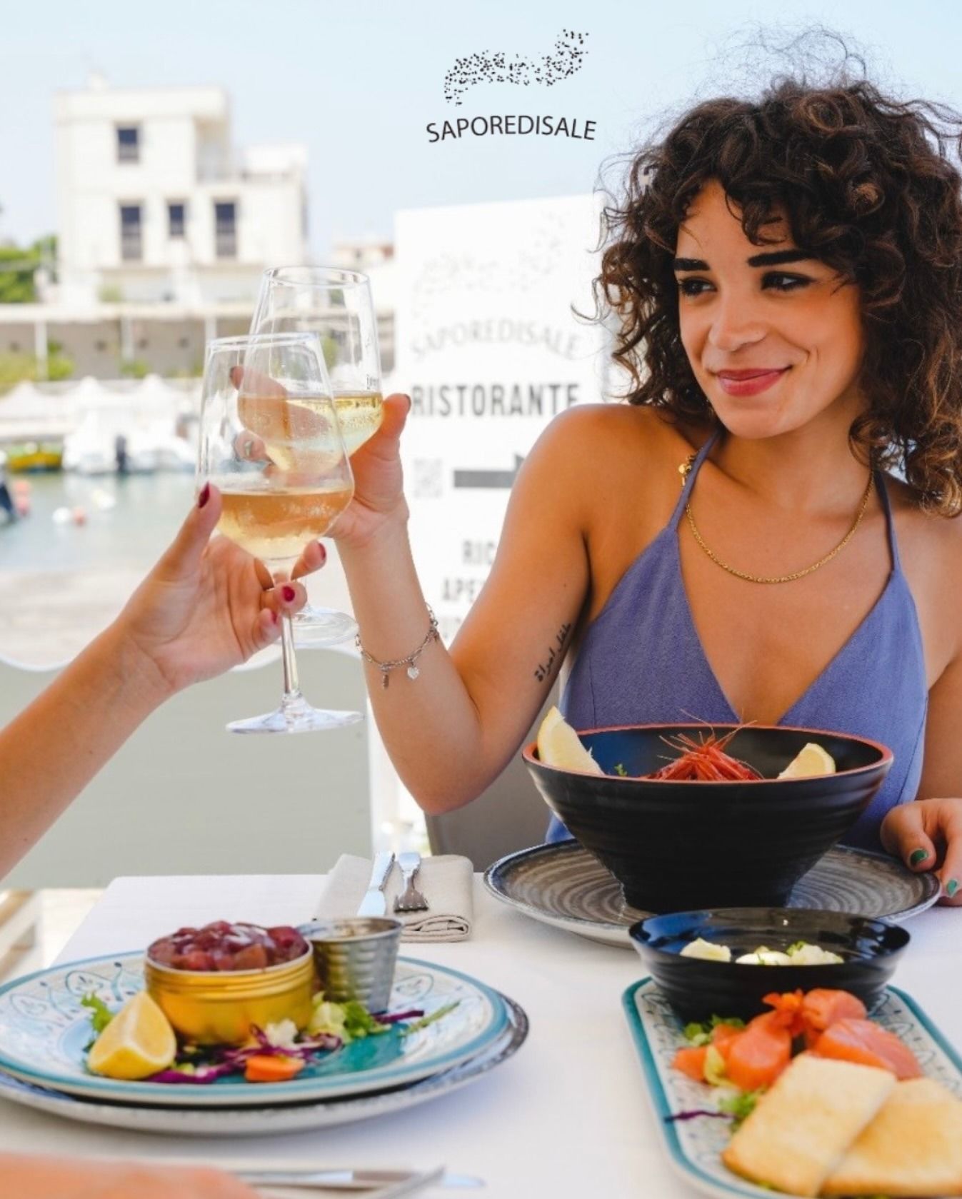 Donna che brinda con del vino in un ristorante sul lungomare che offre un pasto a base di pesce e vista sul porto.