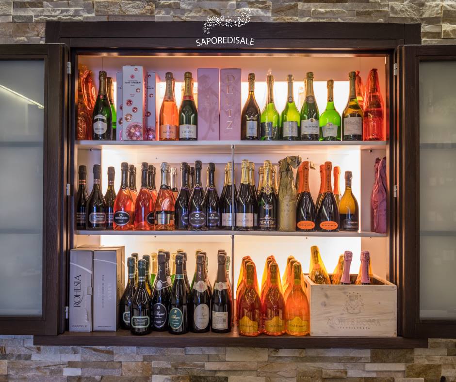 Vetrina piena di bottiglie di champagne in un ambiente ben illuminato con pareti in pietra.