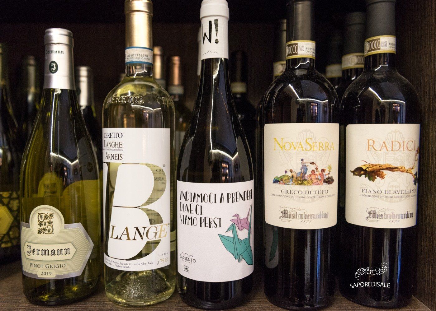 Bottiglie di vino su uno scaffale; le etichette variano a seconda che si tratti di bottiglie di vino nero, bianco o rosso.