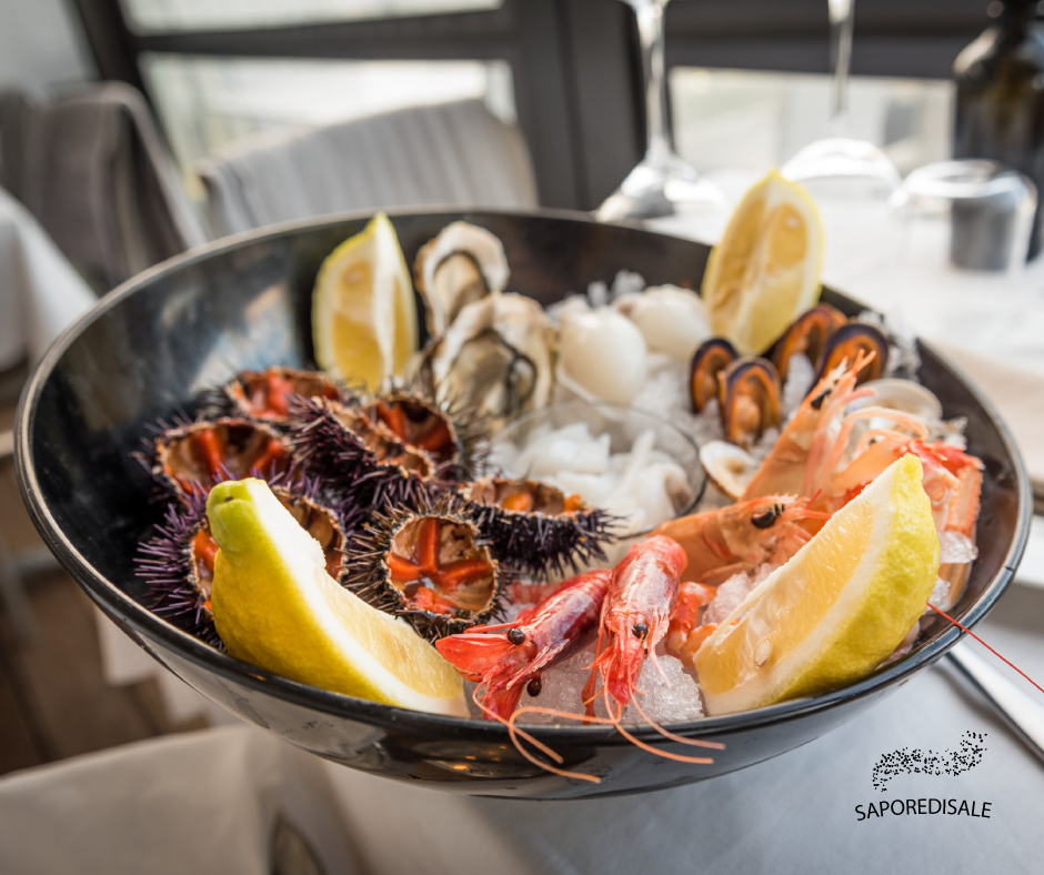 Piatto di frutti di mare: ricci di mare, gamberi, ostriche, cozze, spicchi di limone e ghiaccio in una ciotola scura su un tavolo.