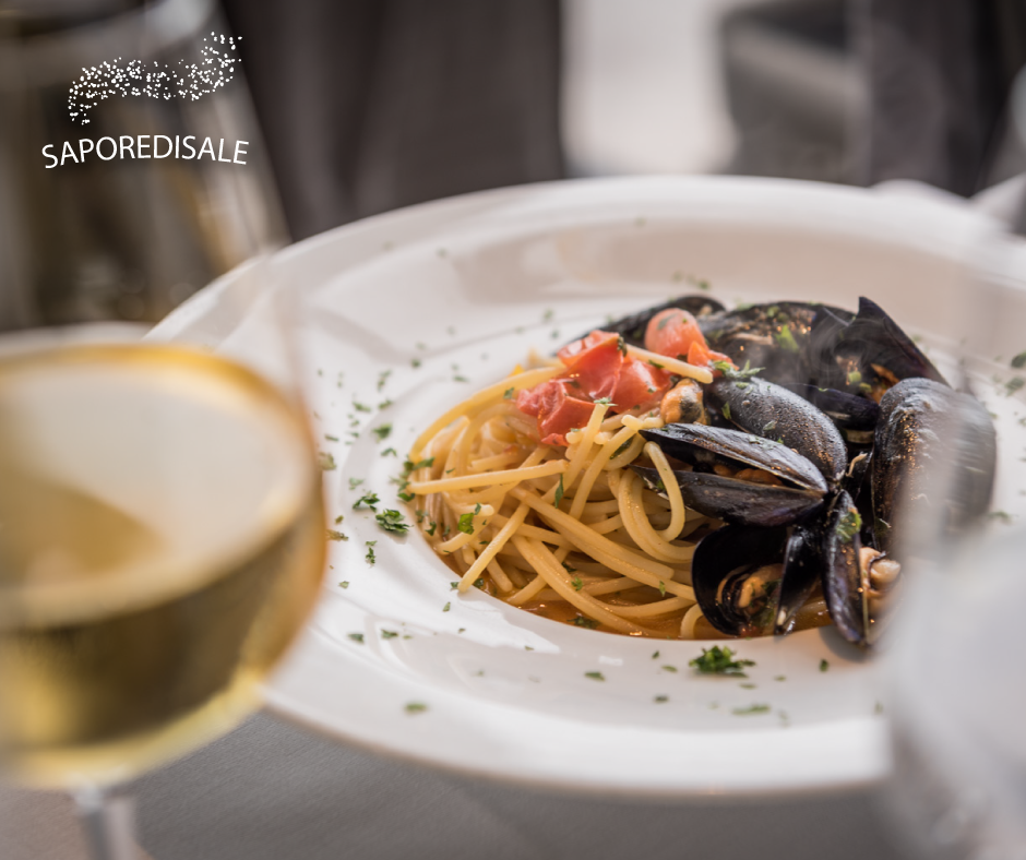 Spaghetti con cozze e pomodori su un piatto bianco, serviti con vino bianco.