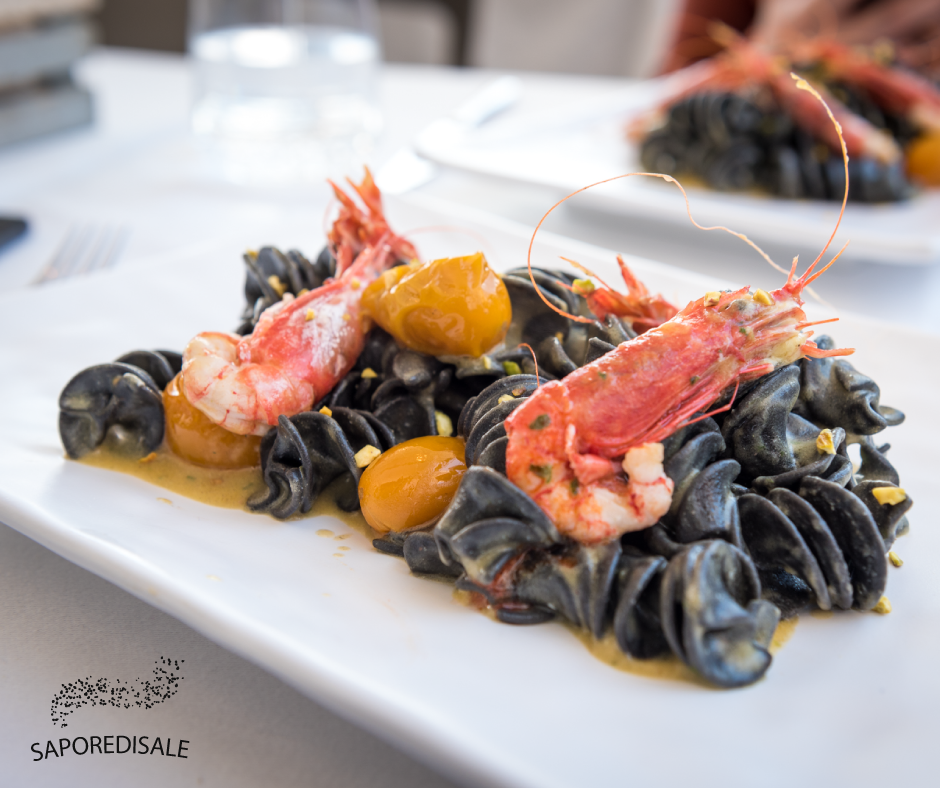Pasta nera con gamberi e salsa all'arancia su un piatto bianco.