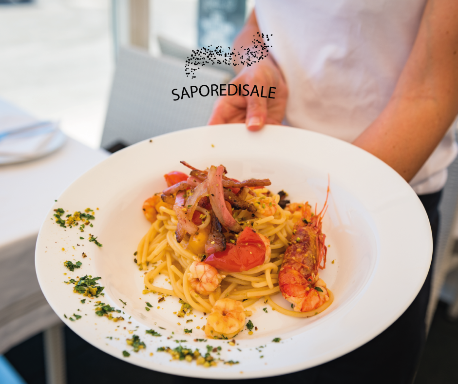 Piatto di pasta con gamberi, pomodori e pancetta, tenuto in mano da una persona.
