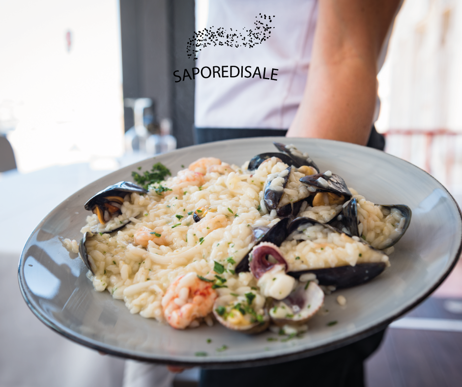 Un cameriere tiene in mano un piatto di risotto ai frutti di mare, con cozze e gamberi, in un ristorante.