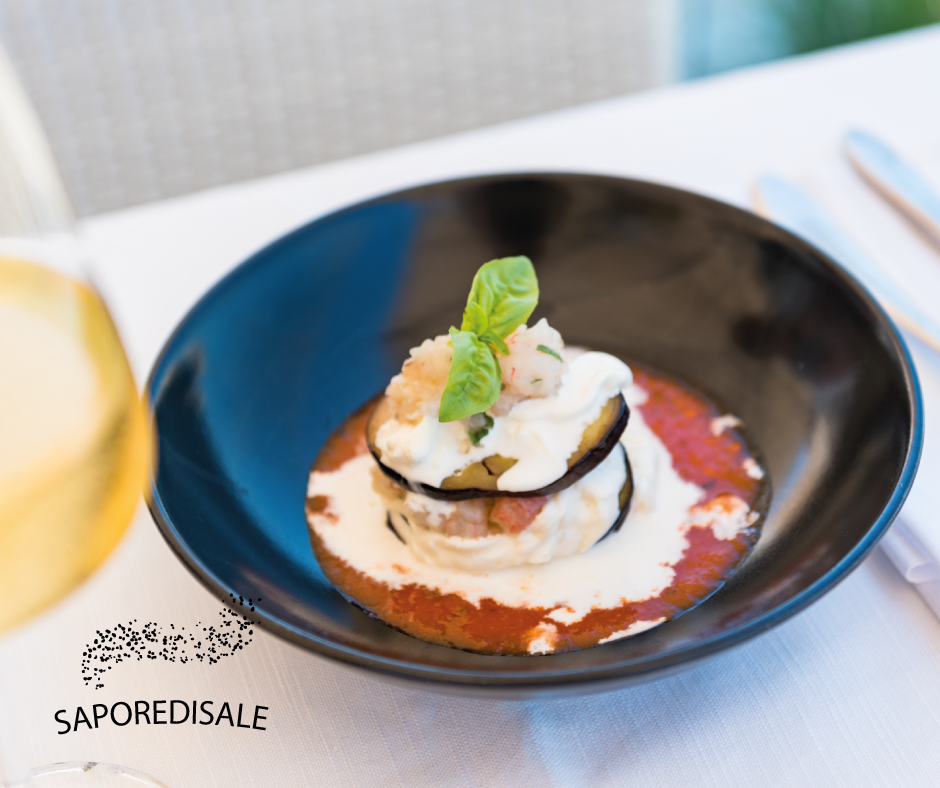 Piatto di melanzane e formaggio in una ciotola nera, servito su una tovaglia bianca.