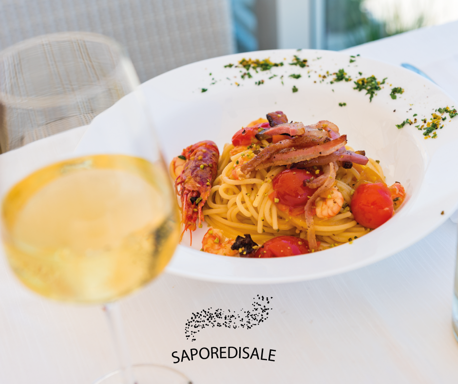 Spaghetti con gamberi, pomodori e polpo in una ciotola bianca, con un bicchiere di vino bianco.