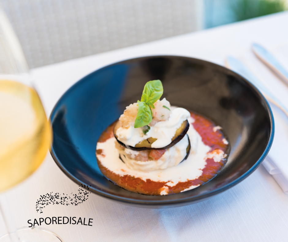 Melanzane a pila con salsa, formaggio e basilico, su un piatto nero.