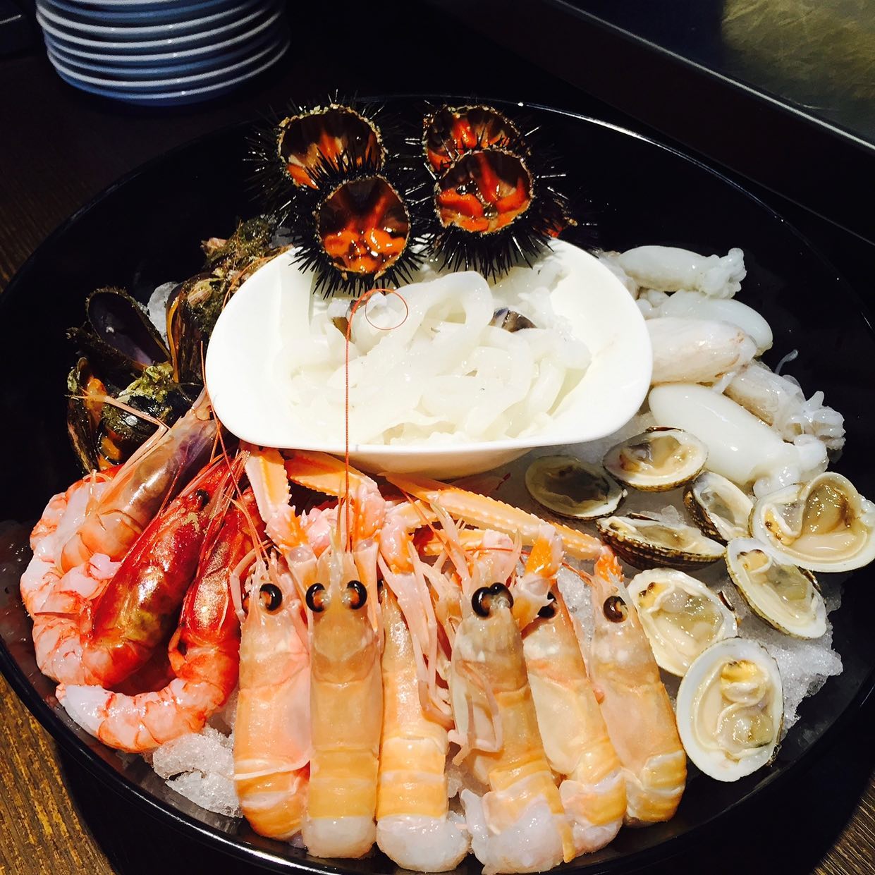 Piatto di frutti di mare: gamberi, aragosta, vongole, calamari e ricci di mare disposti sul ghiaccio in una ciotola nera.