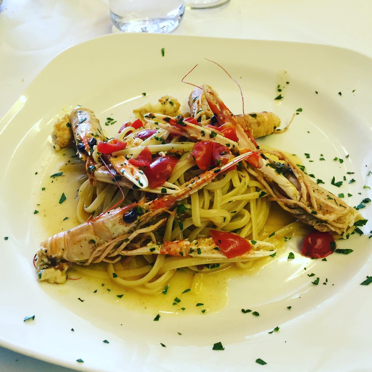 Pasta con gamberi grandi e pomodorini su un piatto bianco.