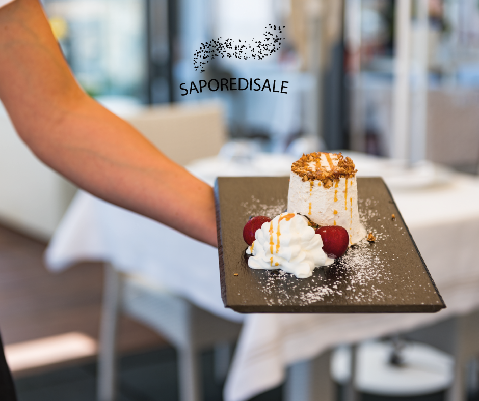 Un cameriere tiene in mano un piatto con un dessert guarnito con panna montata e ciliegie. Ambiente da ristorante.