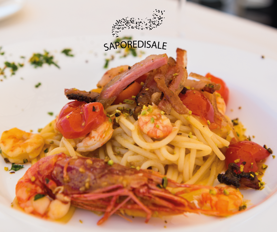 Piatto di spaghetti con gamberi, pomodori, pancetta e pistacchi in una ciotola bianca.