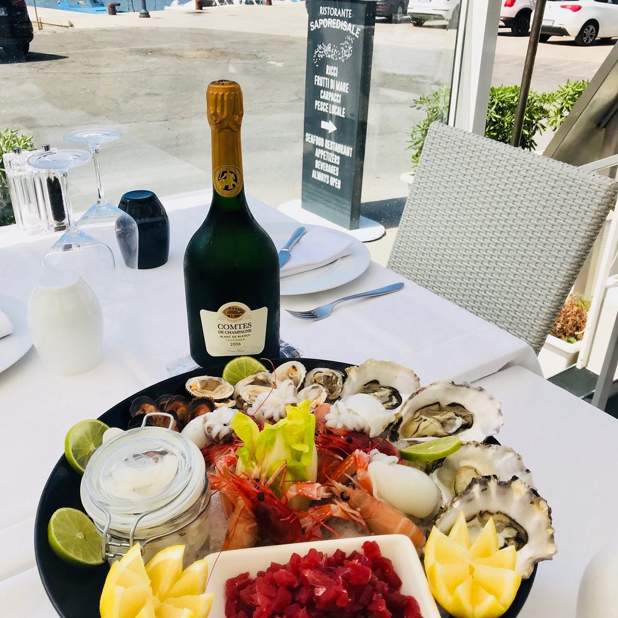 Piatto di frutti di mare con bottiglia di champagne su un tavolo apparecchiato con tovaglie bianche; ristorante all'aperto.